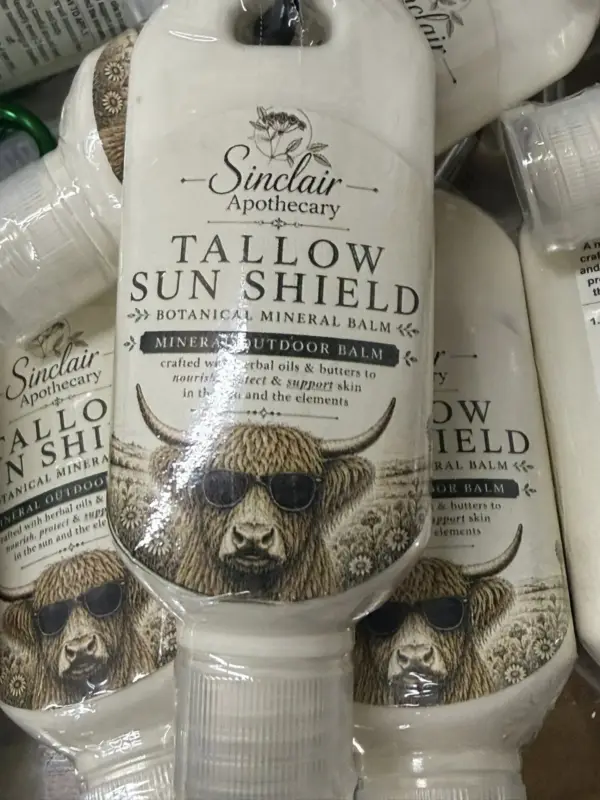 Whimsical Highland cow with sunglasses on natural Tallow Sun Shield skincare bottles, highlighting sun protection benefits.