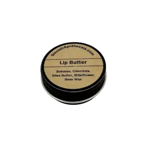 Natural lip balm in a black container with a paper label, featuring nourishing ingredients like shea, beeswax, babassu, calendula, and elderflower.